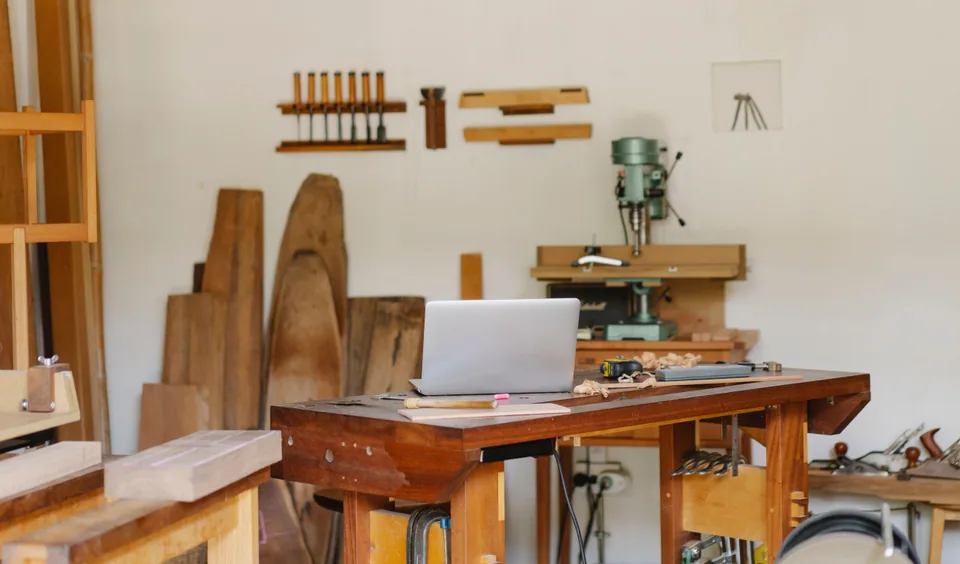 An open laptop and hand tools on a wooden workshop bench. Photo by Ono Kosuki.